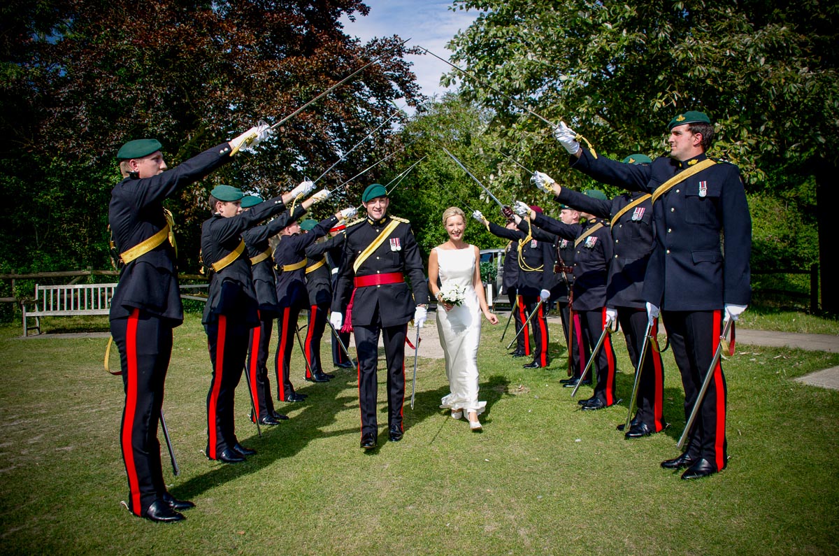  Rachael and Dan walk through a saber arch at their wedding reception at Burpham Village Hall.