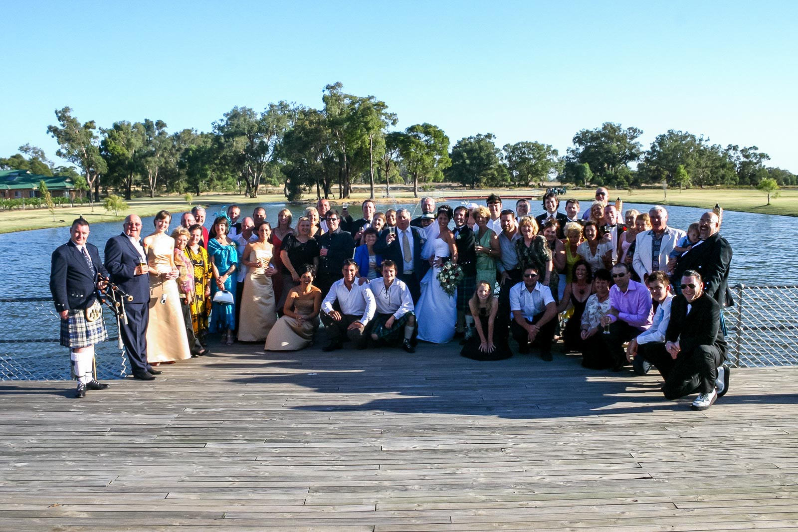 Russ, Megs and their wedding guests pose on front of a lake.