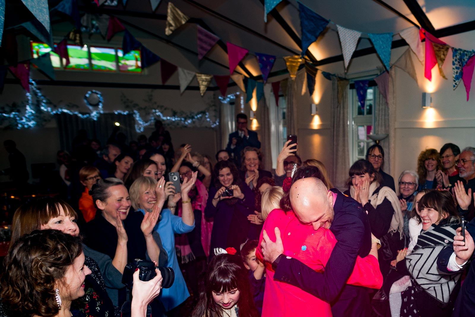 Annie and Mark embrace after their wedding on front of guests in Firle Village Hall.