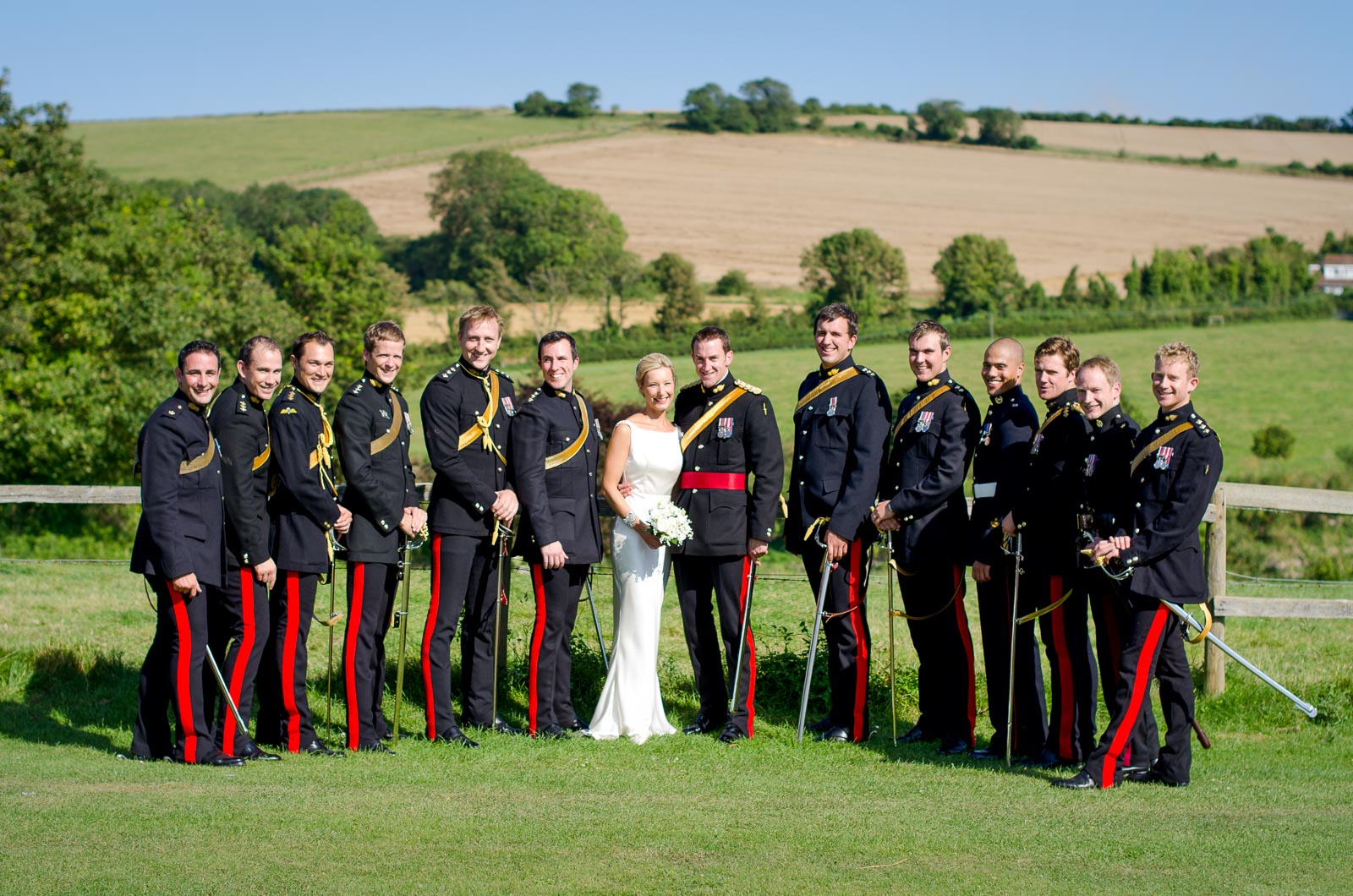 Rachael and Dan pose with Dan's army wedding guests on front of the South Downs during their wedding reception at Burpham Village Hall.