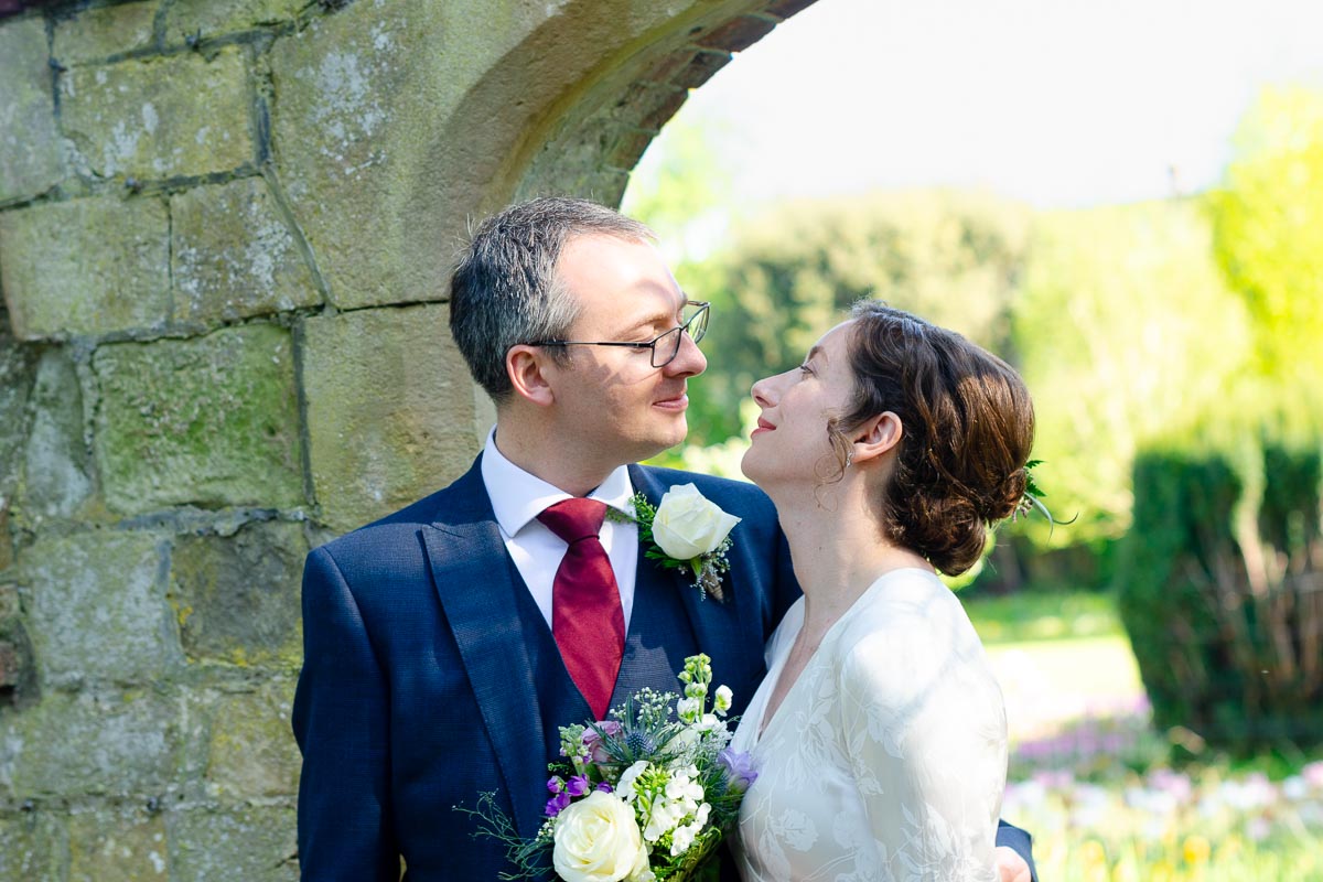 Alexis and Niell smile at eachother on front of one of the arches in Southover Grange after their wedding.