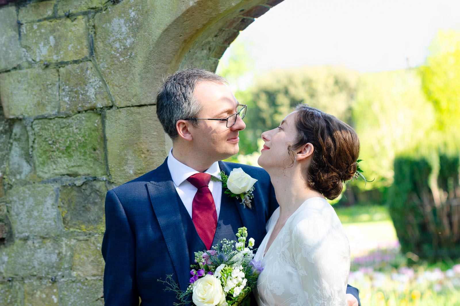 Alexis and Niell smile at eachother on front of one of the arches in Southover Grange after their wedding.
