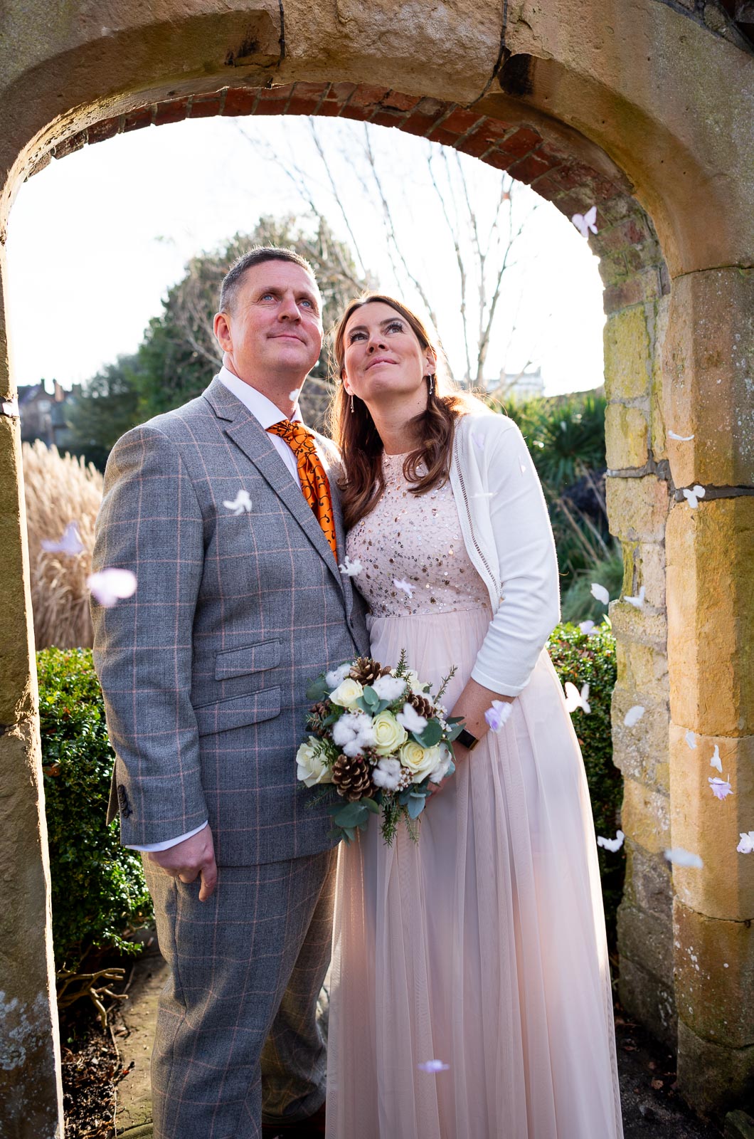 Grant and Jane stand in one of the arches at Southover Grange in Lewes surrounded by confetti.