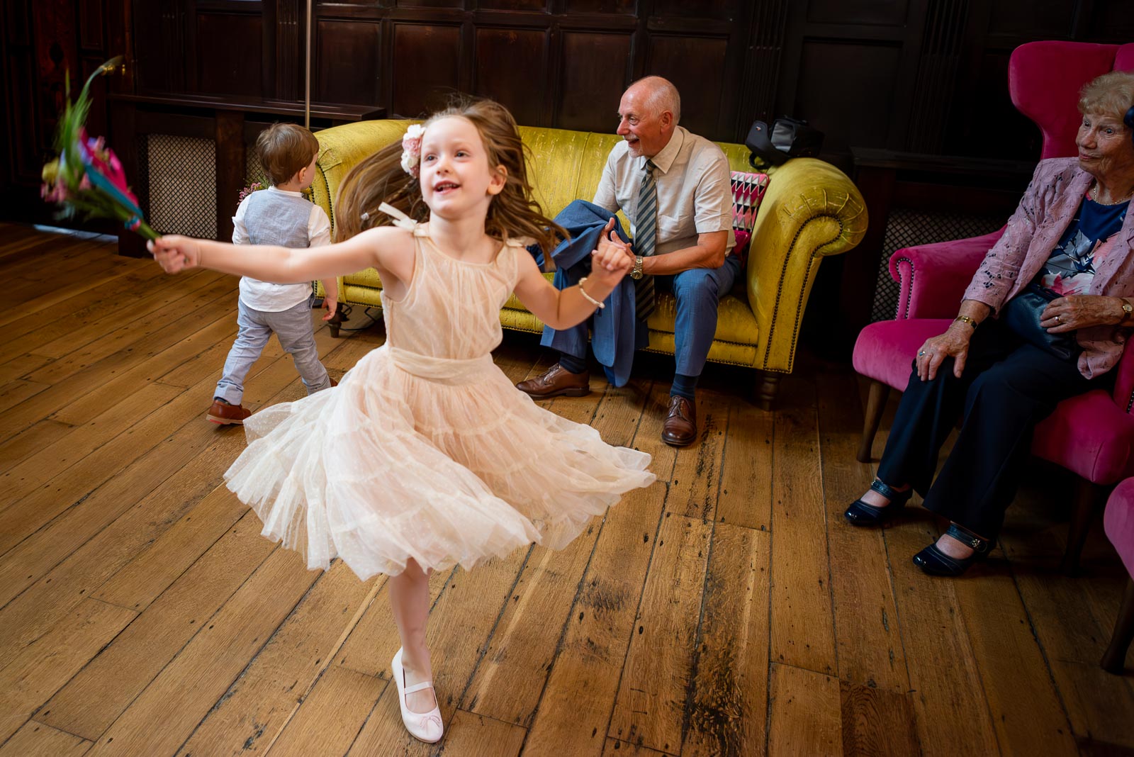 A young bridesmaid twirls with bouquet in hand in the entrance hall of Lewes Register Office.