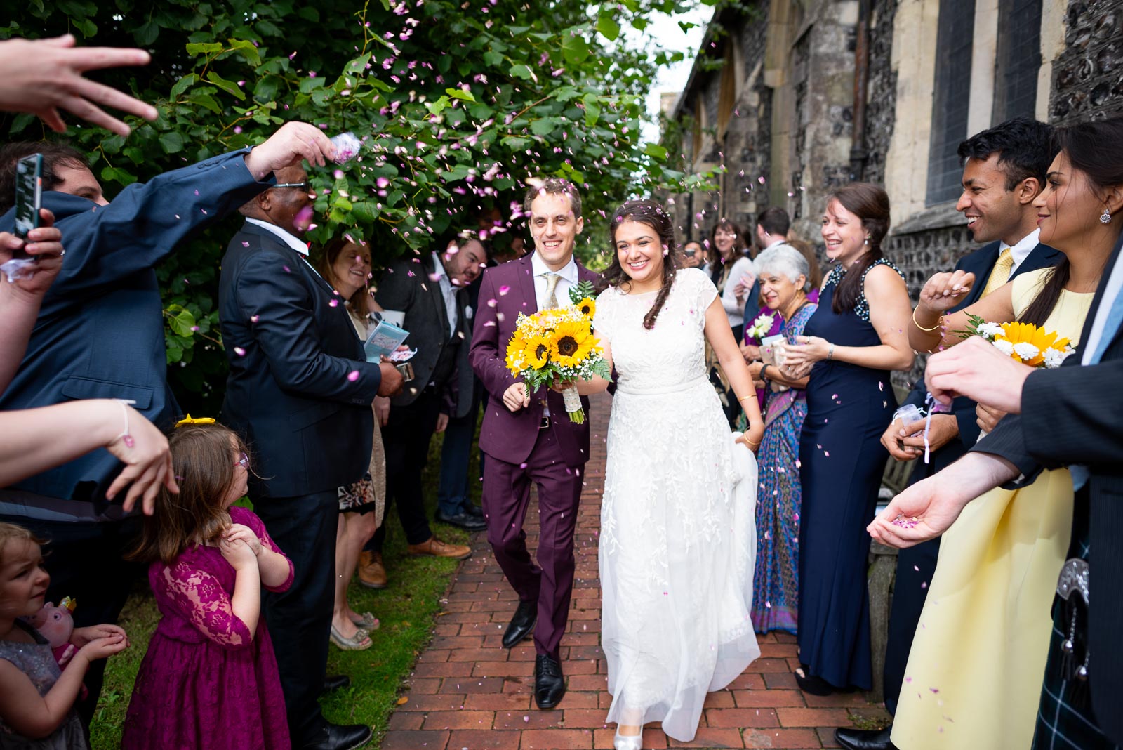 Ashley and Anjana are showered with confetti thrown by their guests outside Trinity Church, Lewes after their wedding.