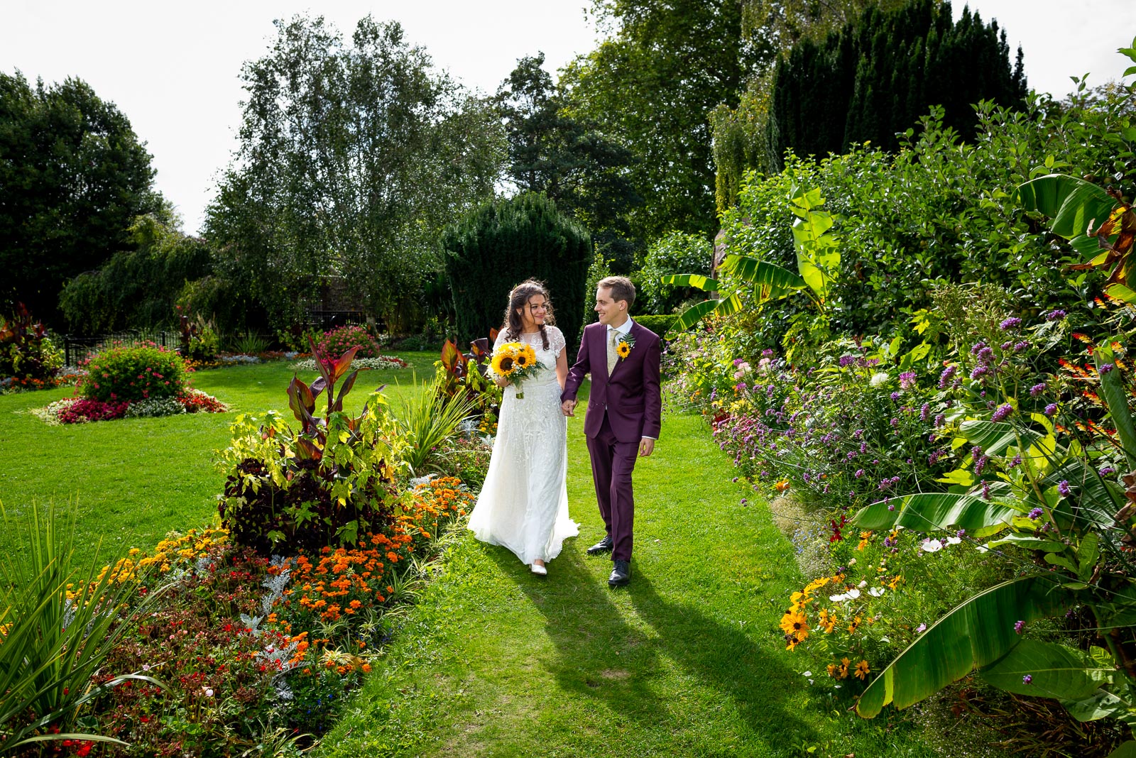 Ashley and Anjana walk between the blooming flower beds in Southover Grange, Lewes after their wedding.