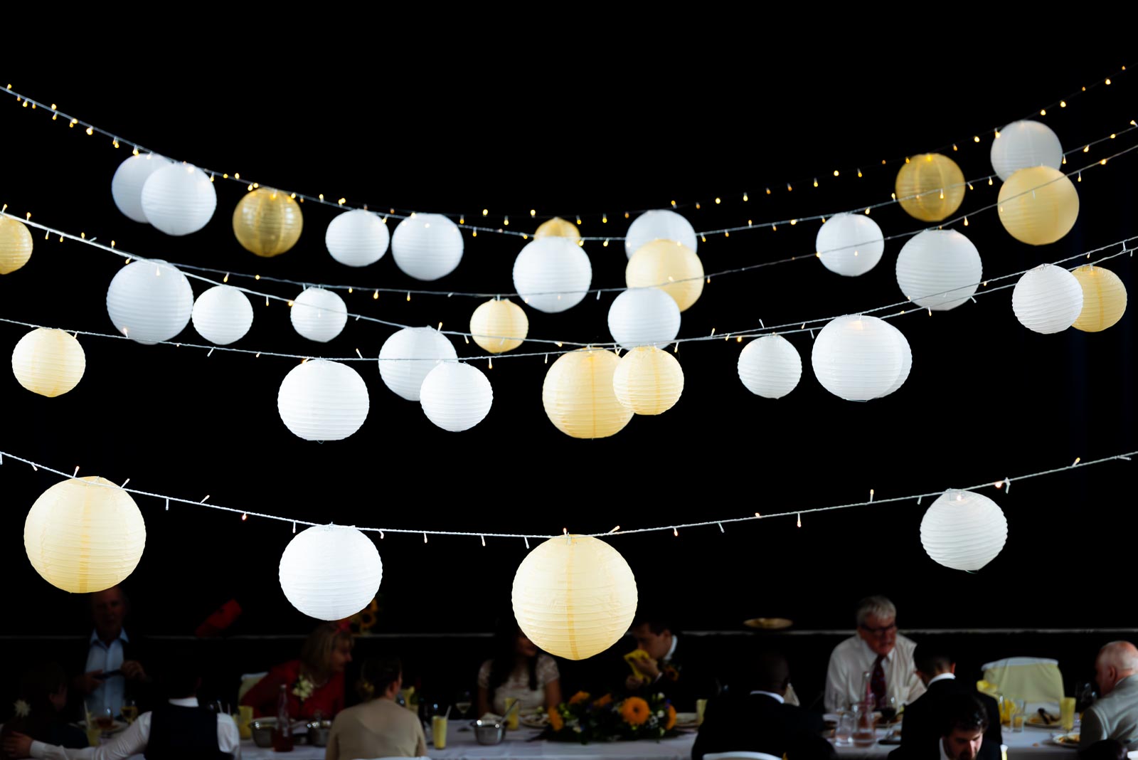 Glowing lantern lights illuminate the high ceiling at Ashley and Anjana's Wedding Reception in Lewes All Saints Centre.