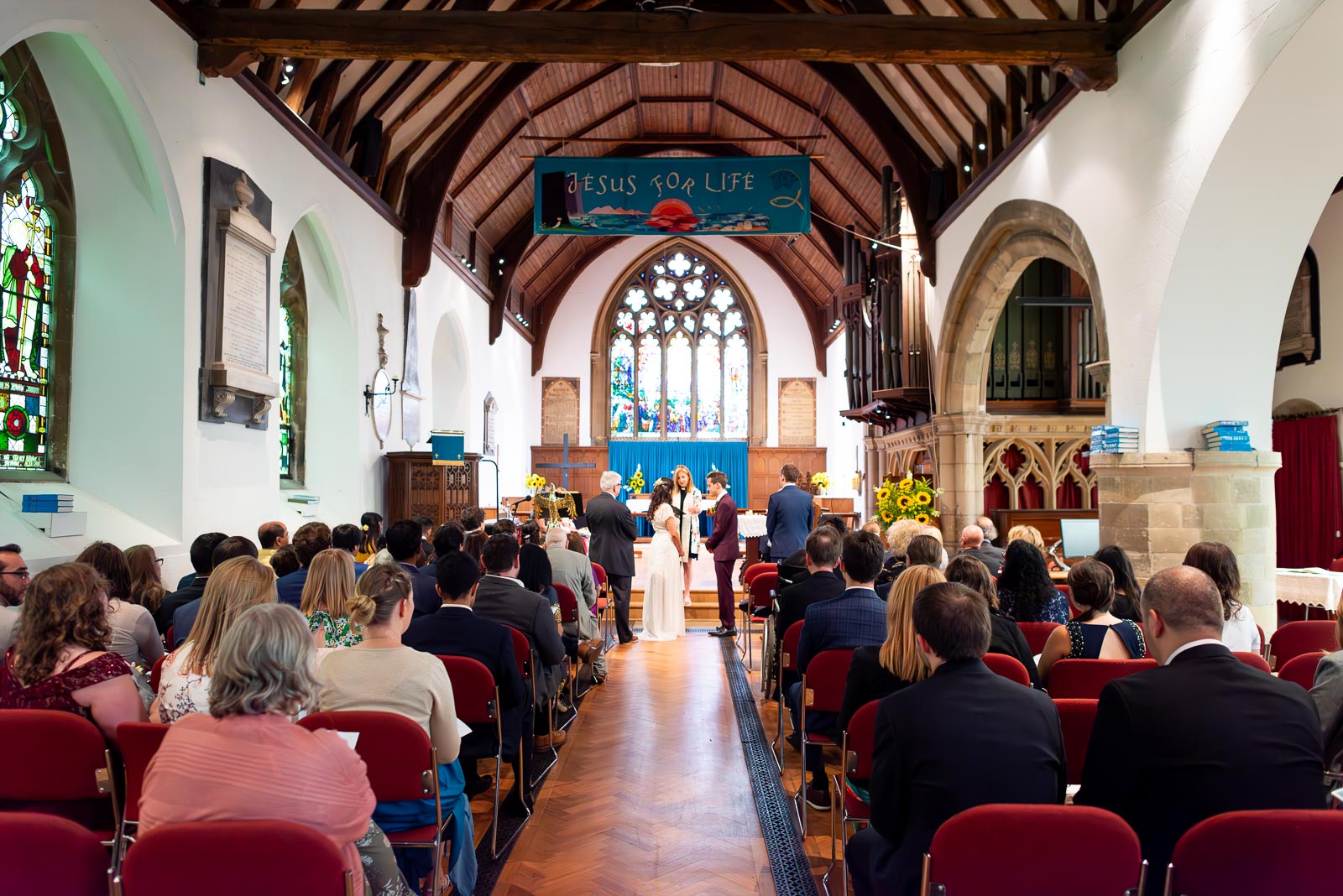 Ashley and Anjana look at eachother  surrounded by wedding guests during their wedding in Trinity Church, Lewes.