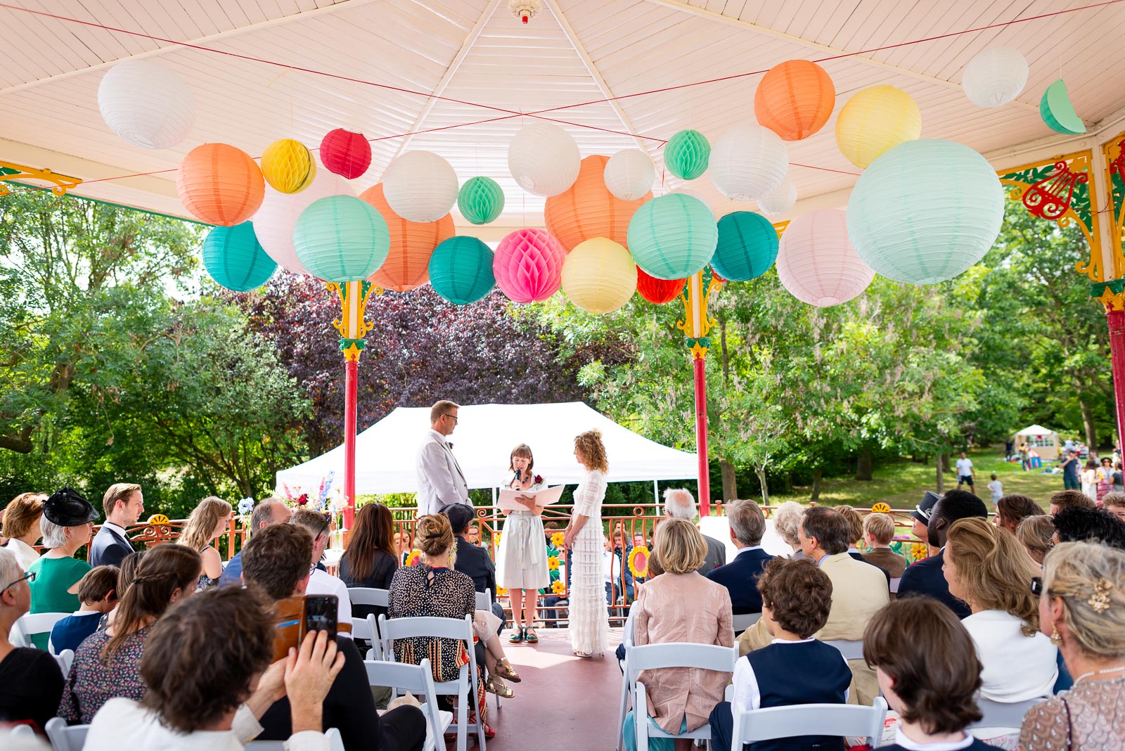 Kitty and Will face eachother surrounded by their Wedding Guests at the Band Stand in Queens Park. 