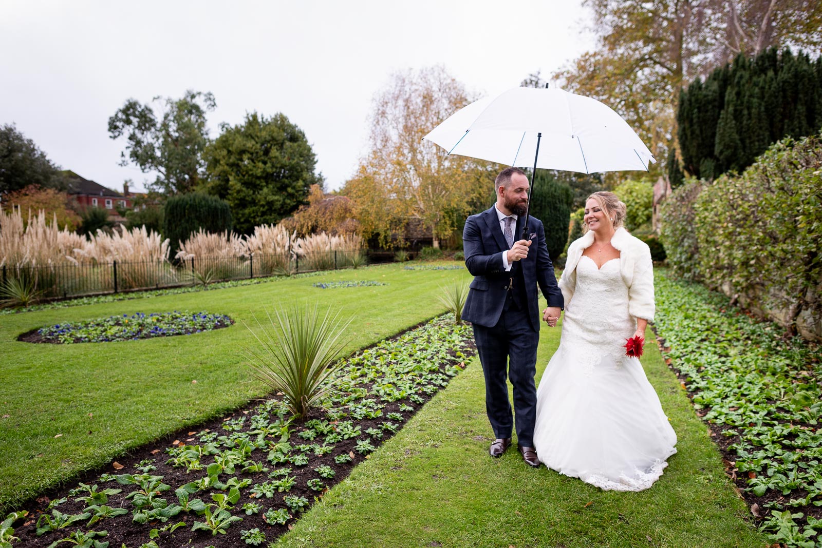 Laura and Sam walk inbetween the flowerbeds in Southover Grange, Lewes after their wedding. 