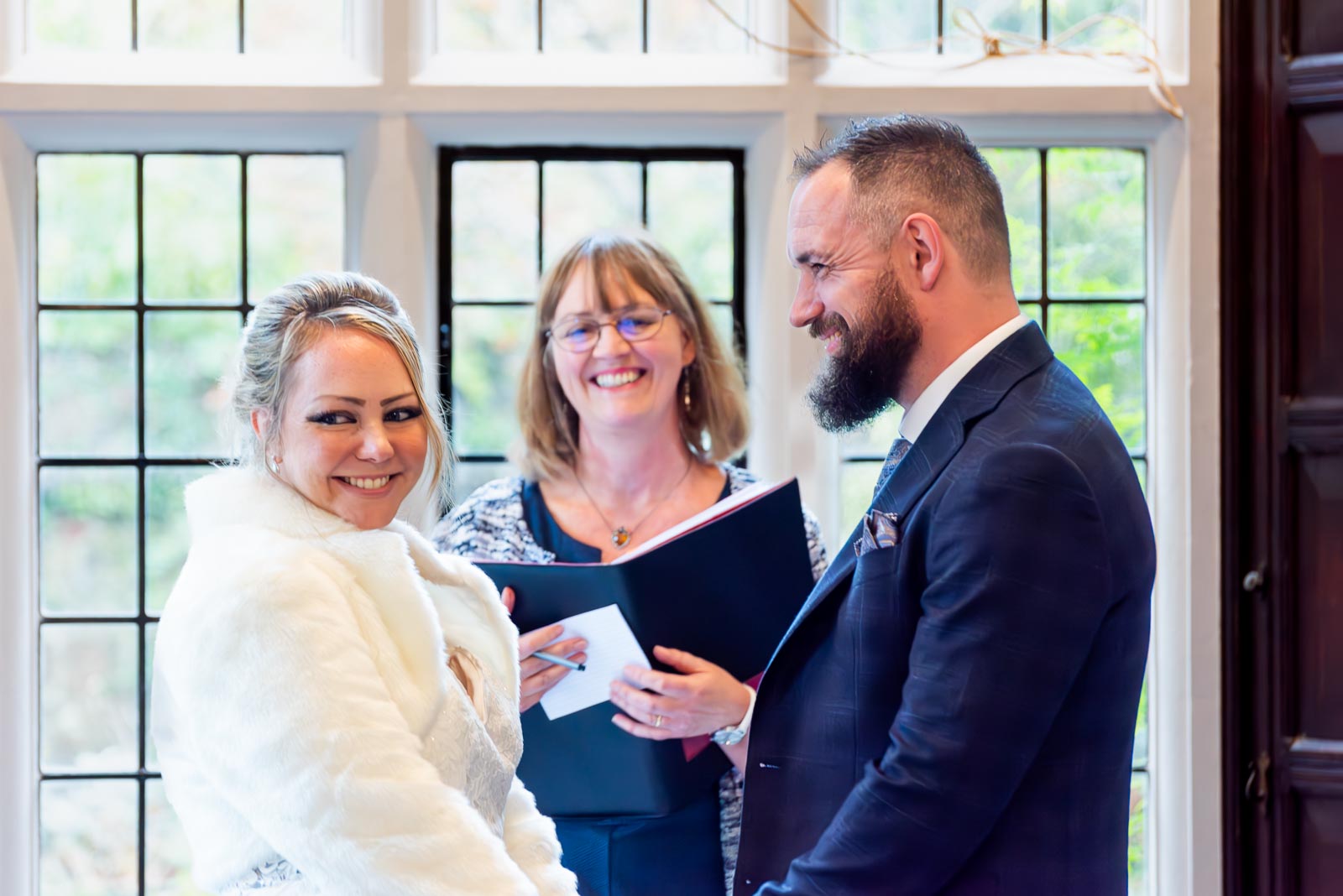 Laura smiles at her wedding guests at the top of the aisle in the Ainsworth Room in Lewes Register Office during their wedding.