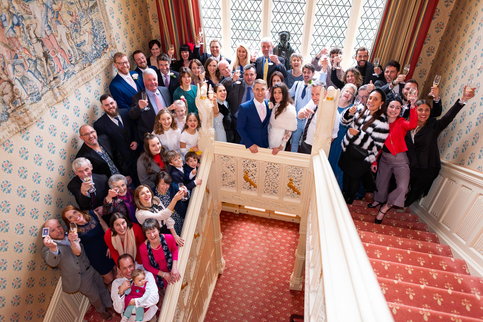 Virgina, Simon and their guests pose for a photo on the stairs at Horsted Place during their wedding reception.