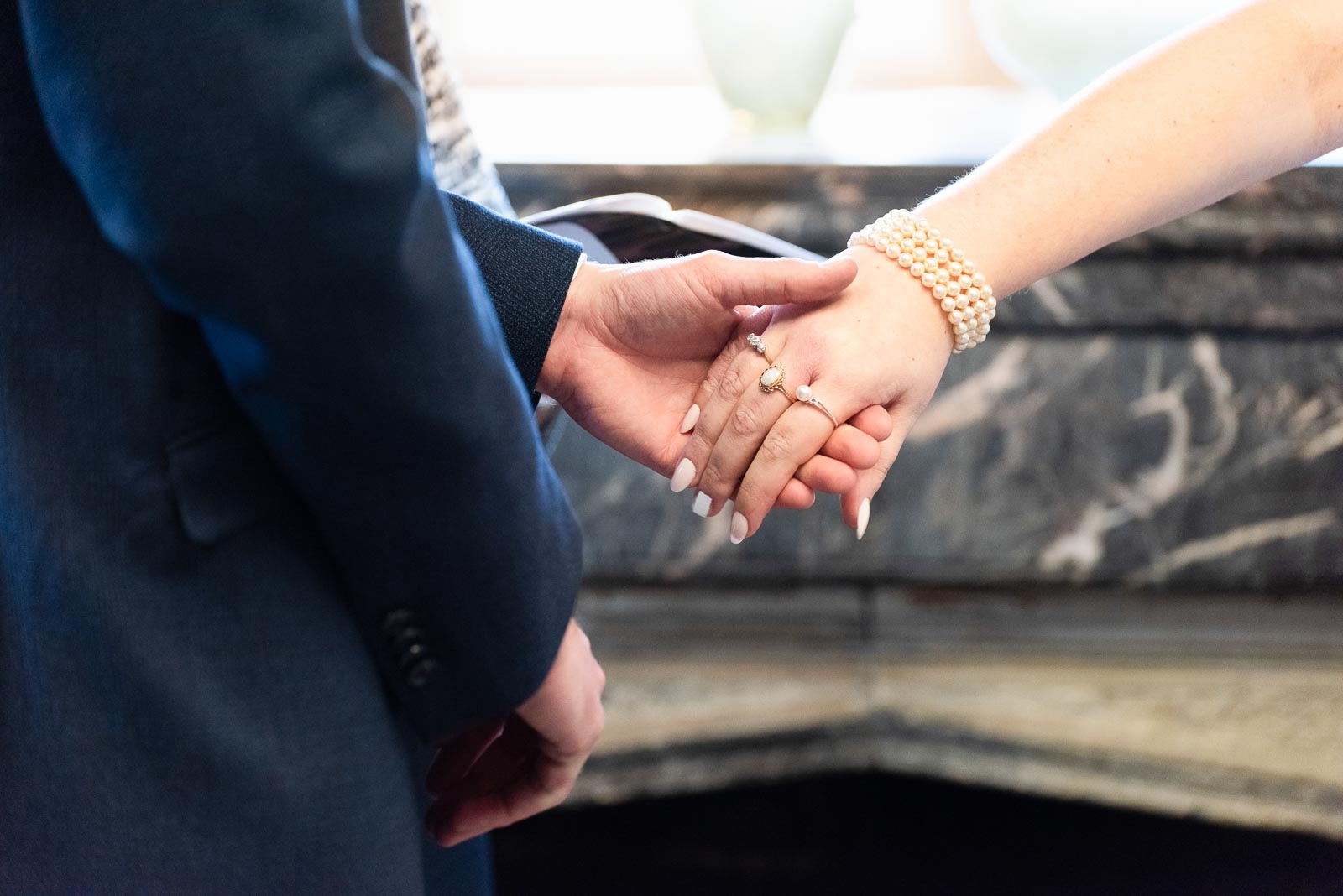 A close up of Chris holding Belinda's hand in the Evelyn Room at Lewes Register Office during their wedding.