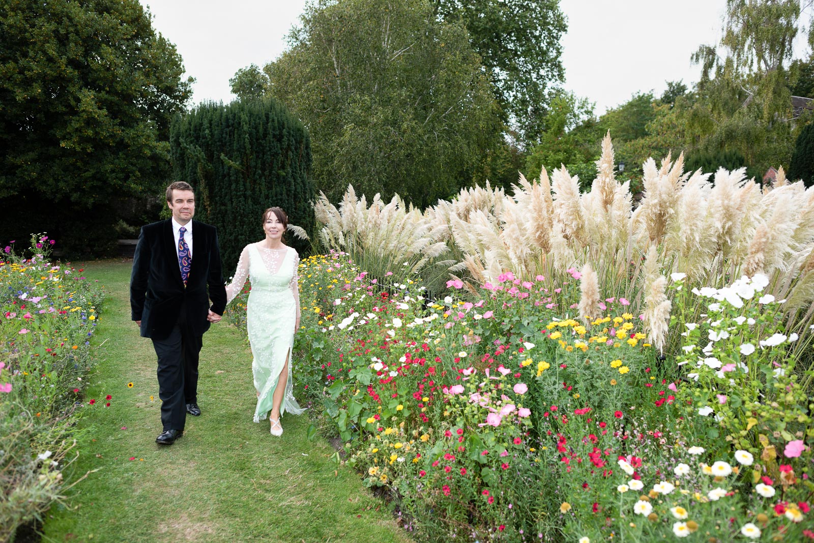 Fiona and Richard walk between the flower beds at Southover Grange in Lewes after their wedding.