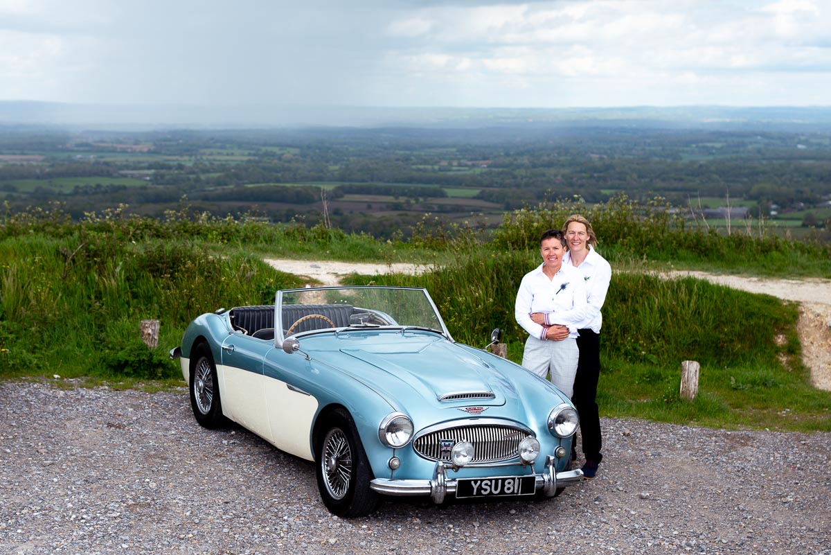 Kate and Sam pose next to their wedding car at Ditchling Beacon.