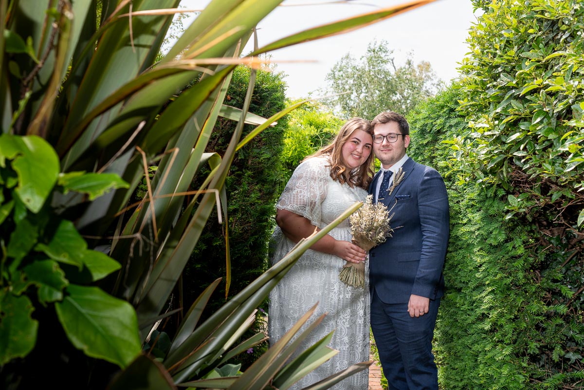 Sophie and Nathan smile through the plants at Southover Grange after their wedding in Lewes Register Office.