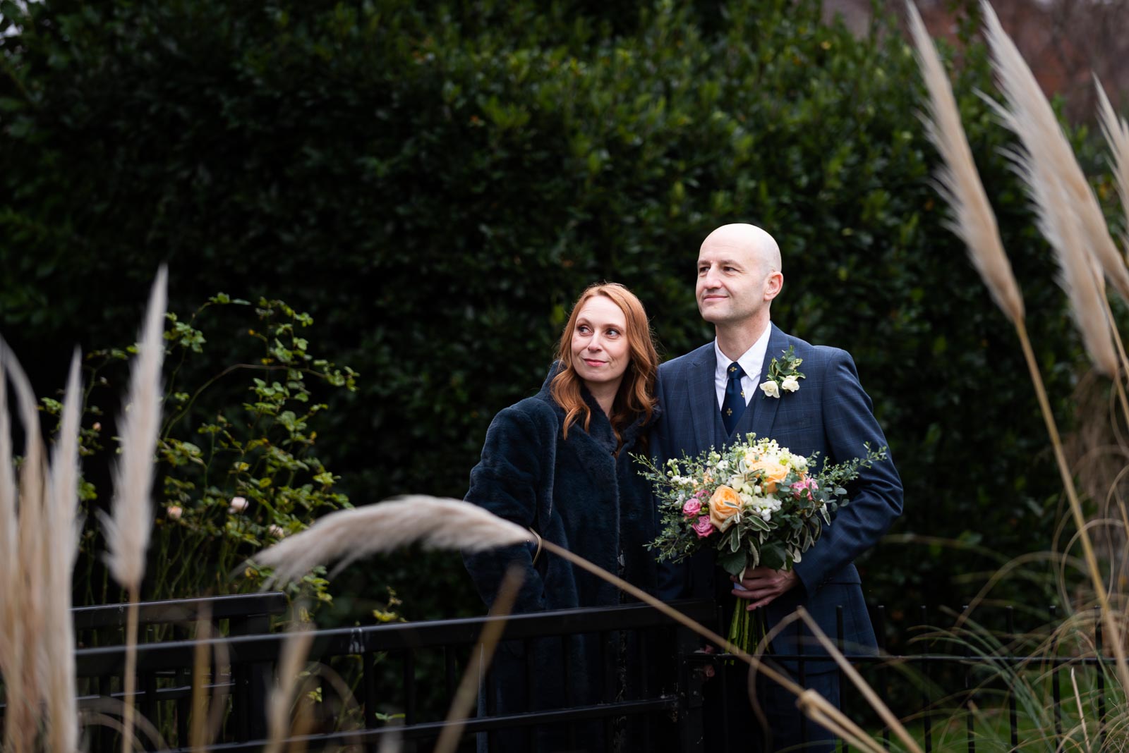Melanie and Ryan smile through some tampa grass in Southover Grange after their wedding at Lewes Register Office.