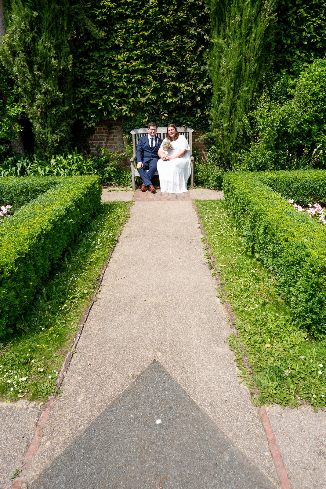 Sophie and Nathan pose on one of the benches in the secret garden in Southover Grange after their wedding in Lewes Register Office.
