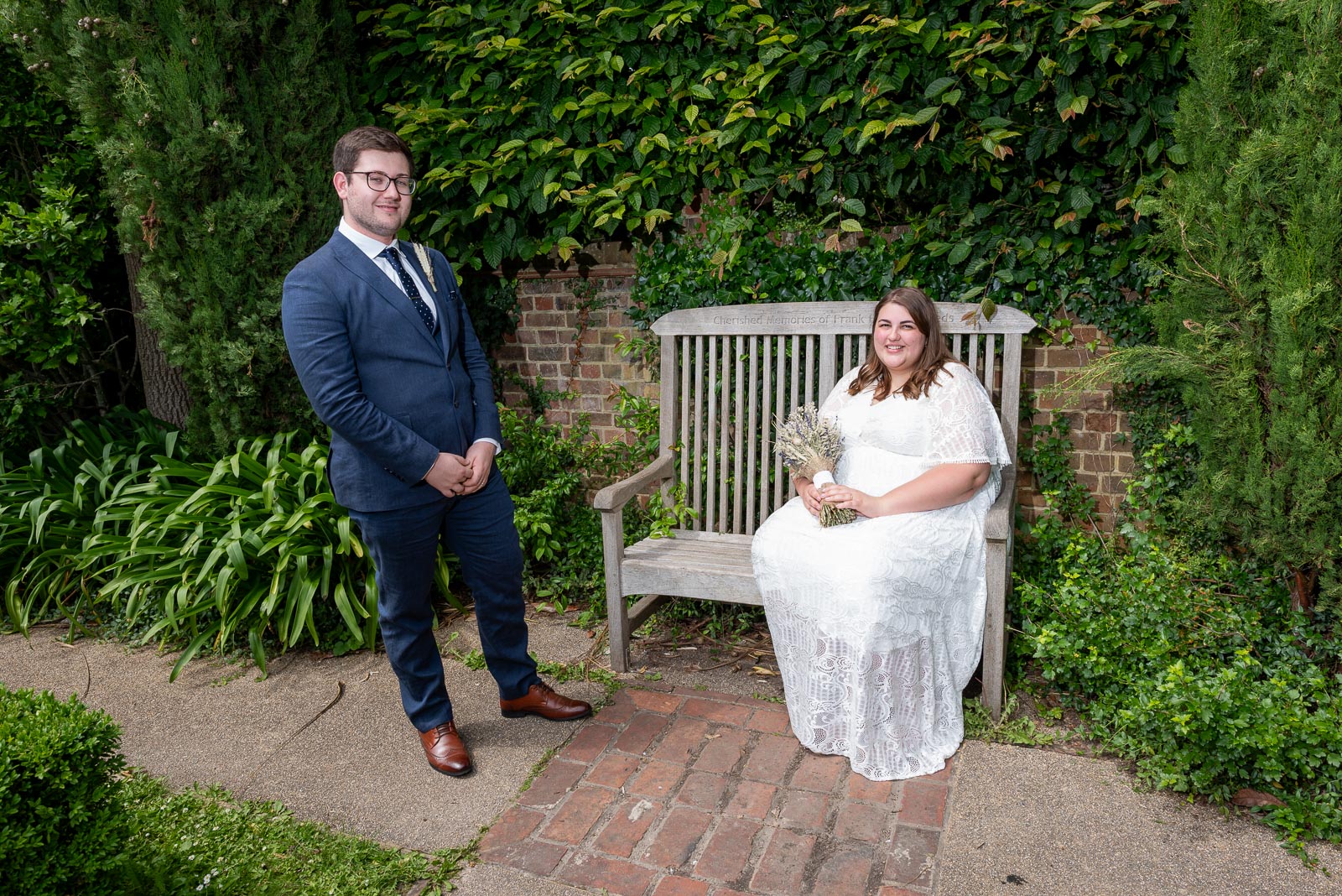 Sophie and Nathan pose on one of the benches in the secret garden in Southover Grange after their wedding in Lewes Register Office.