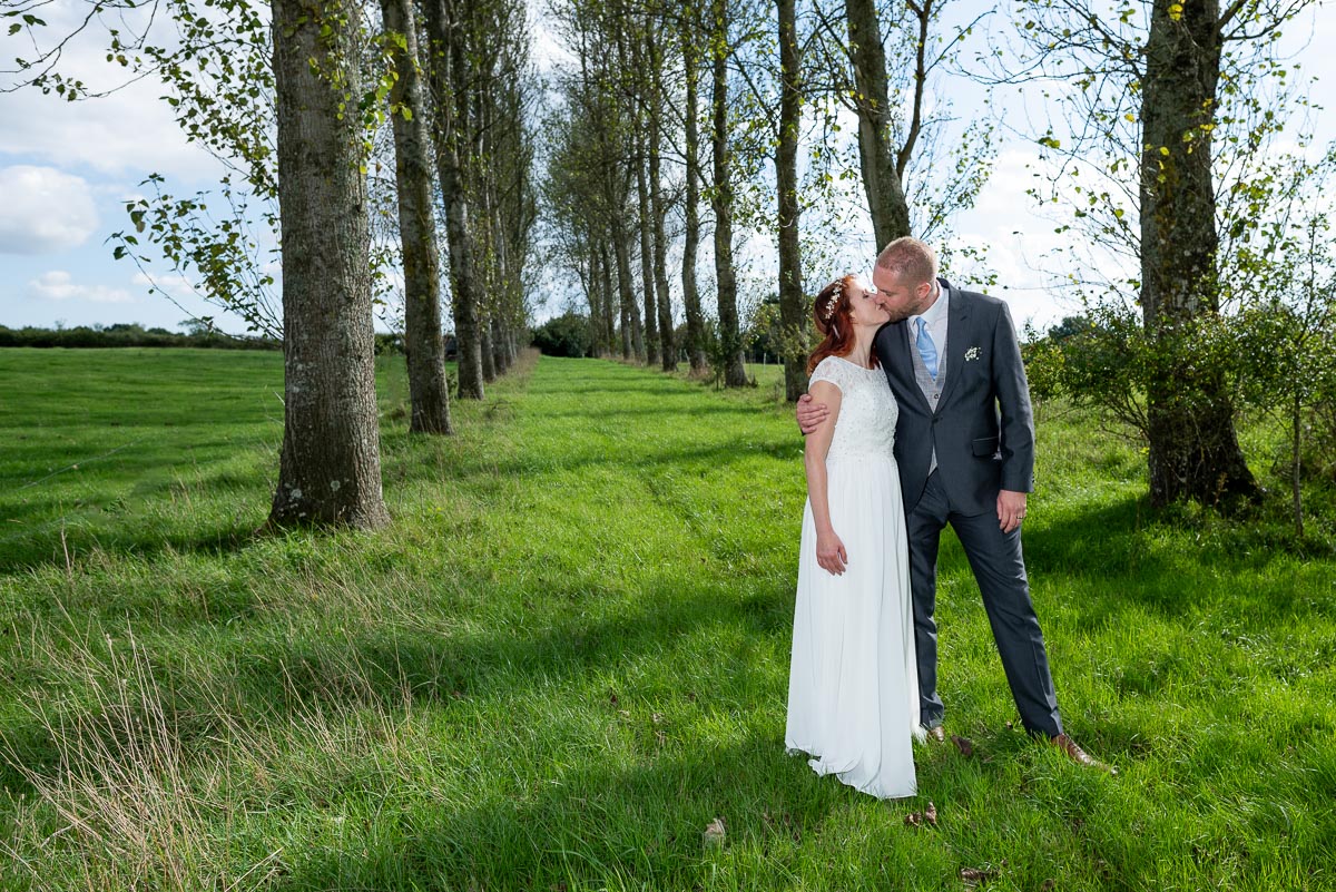 Adrienn and Lee embrace on front of a line of trees  on the grounds of Milward Farm near Lewes after their Wedding on the estate.