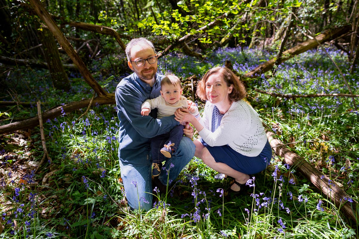Alexis and Niell crouch down among the bluebells with their eight month old baby Alasdair among the bluebells at Battle Great Woods.