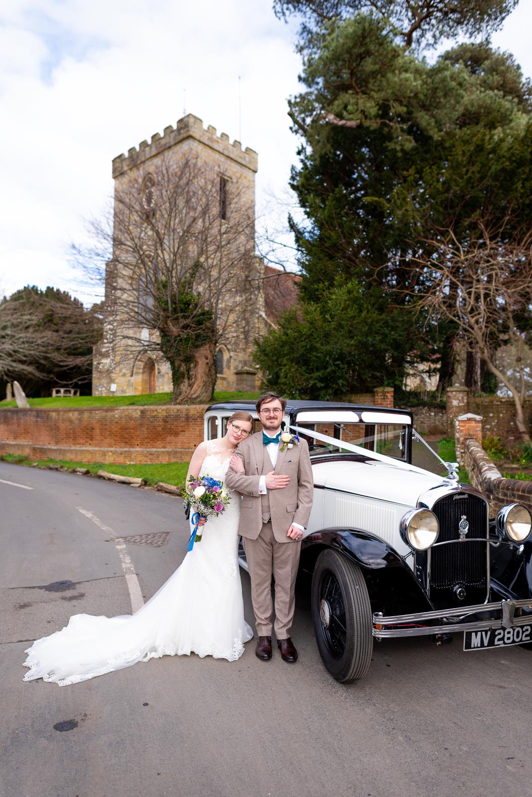 Lewis and Stephanie pose next to their wedding car outside The Church of St Peter and St Paul in Hellingly. 
