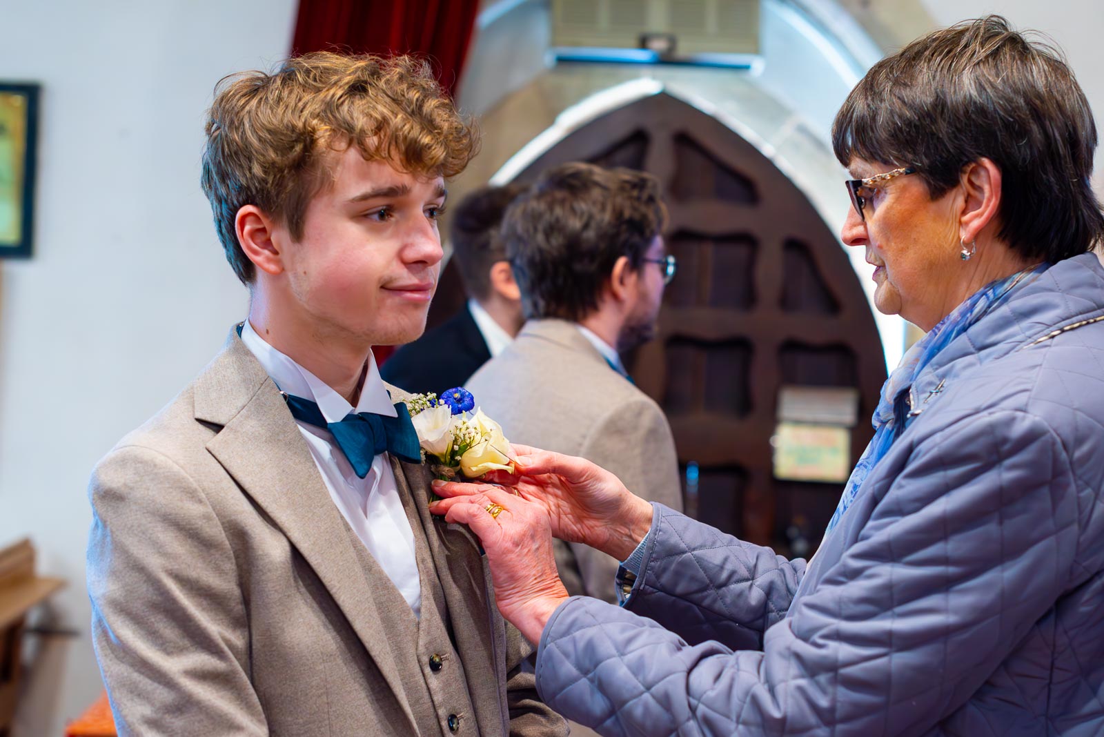 Stephanie's brother recieves a bit of help with his wedding pin from an auntie before Stephanie's Wedding in The Church of St Peter and St Paul in Hellingly. 