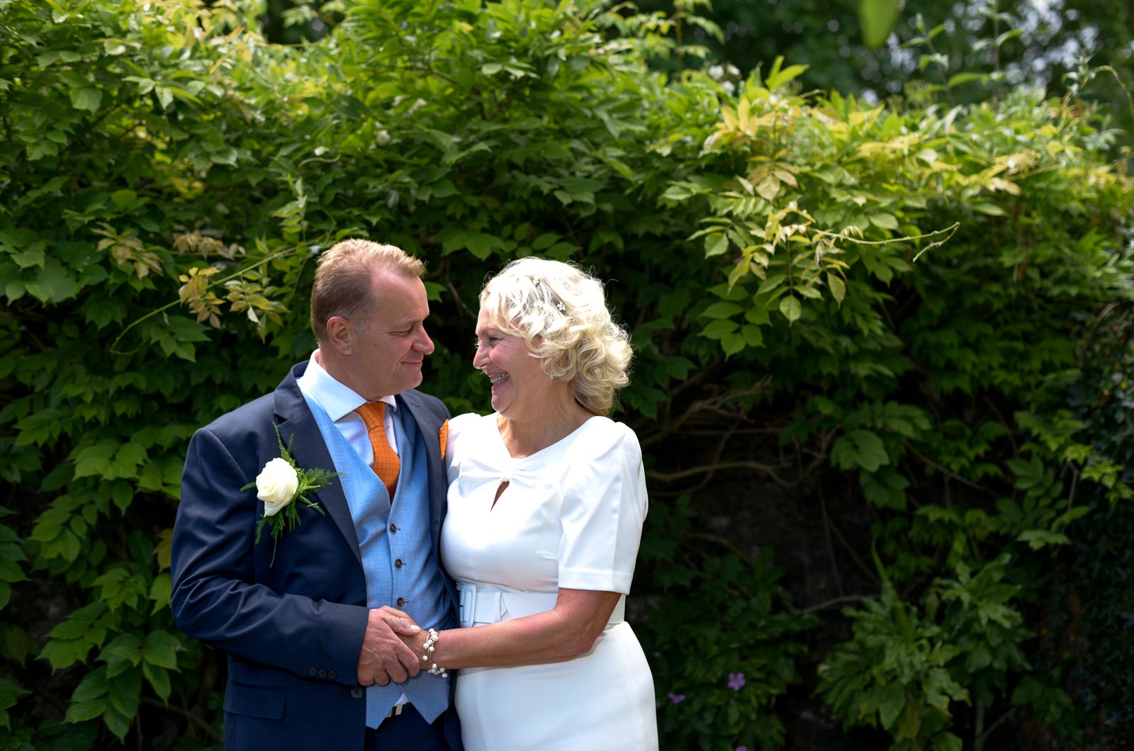 Martin and Joanne smile at each other on front of some lush green bush in Southover Grange after their wedding.