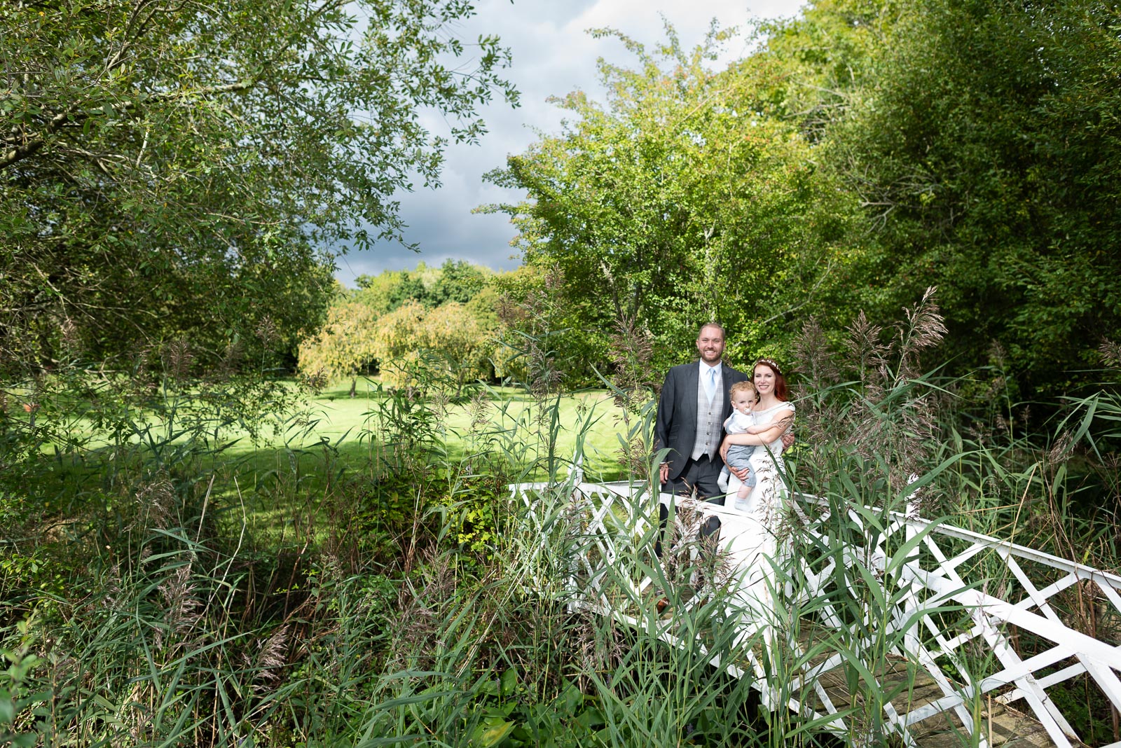 Adrienn, Lee and their youngest son pose on the white lattace bridge at Milwards Farm Estate near Lewes after their wedding