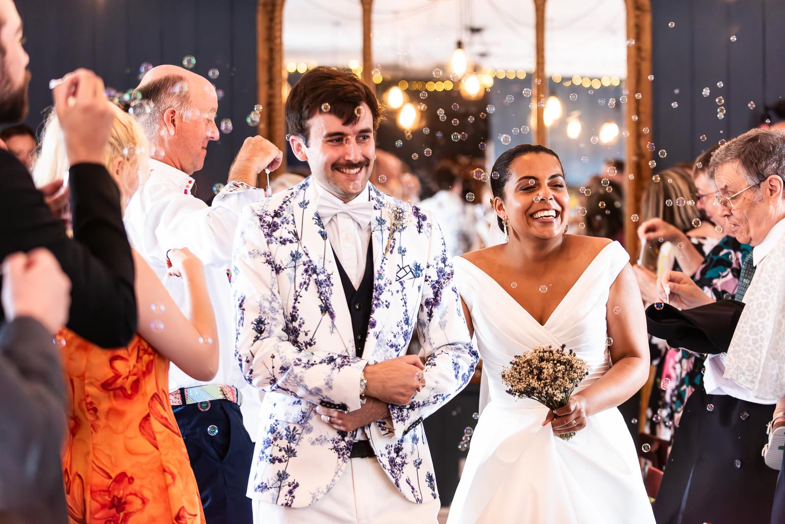Olivia and Edward walk through bubble confetti blown by their wedding guests after becoming husband and wife at the function room at The Royal Oak in Lewes surrounded by friends and family.
