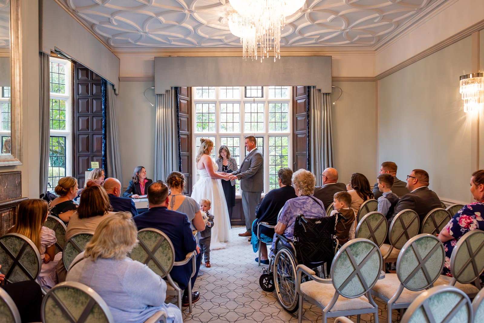 Eliana and Jacob exchange vows with their all their guests present at the top of the aisle in the Ainsworth Room at Lewes Register Office.