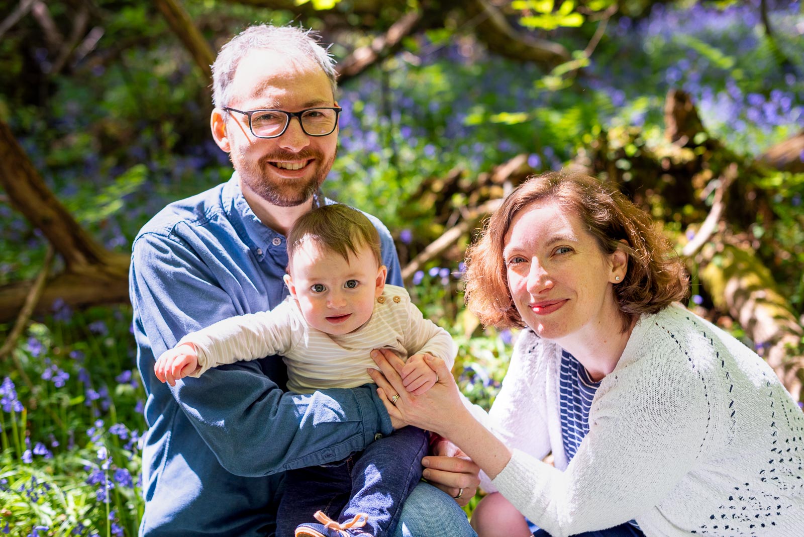 Alexis and Niell crouch down among the bluebells with their eight month old baby Alasdair among the bluebells at Battle Great Woods.