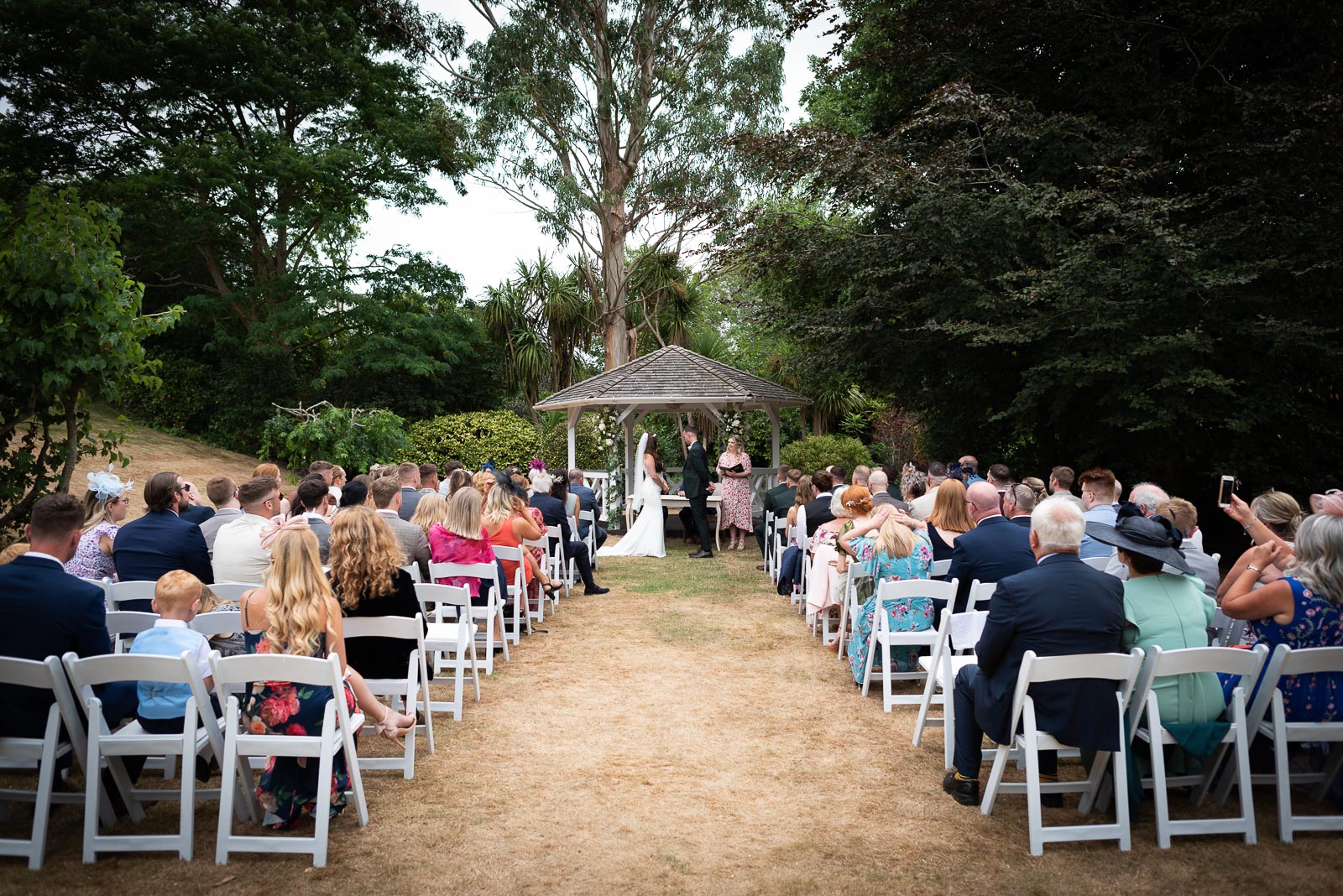 Natalie and Dean exchange vows at their wedding on front of the Gazebo in the garden at Pelham House Hotel, Lewes surrounded by friends and family. 