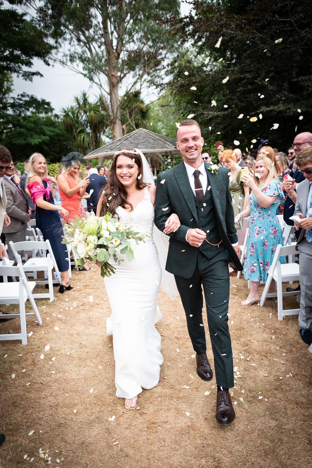 Natalie and Dean walk through petal confetti thrown by their guests after their wedding on front of the gazebo in the garden at Pelham House Hotel, Lewes. 