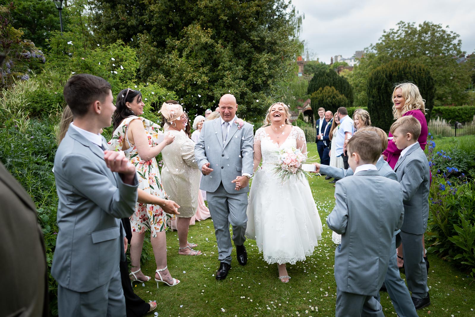 Lou laughs as her and Matt walk through rose petal confetti thrown by friends and family at Southover Grange Lewes.
