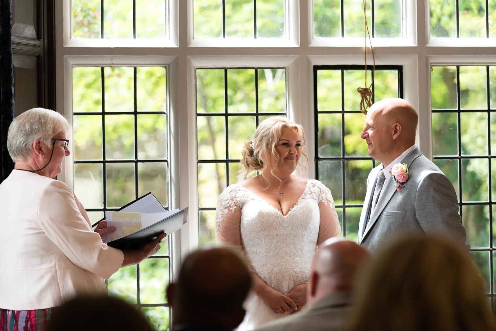 Lou and Matt smile at eachother at the top of the aisle in the Ainsworth Room at Lewes Register Office.