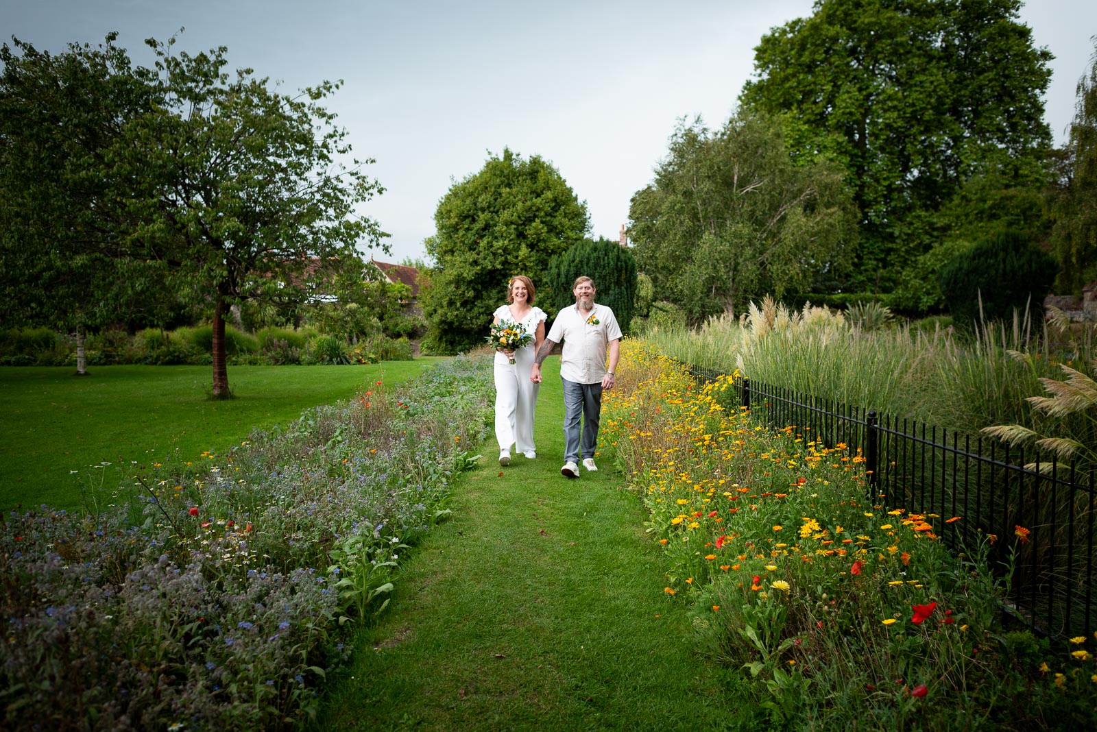 Mary and Mark walk between two flower beds in full bloom at Southover Grange in Lewes
