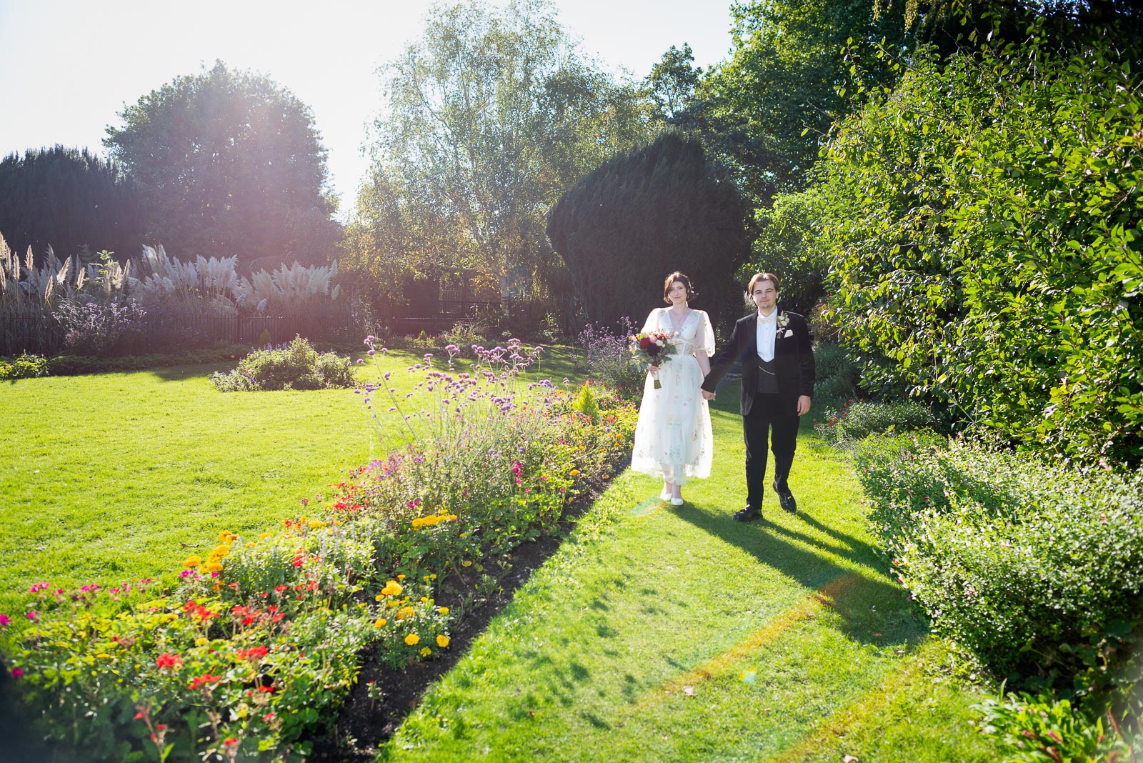 Lola and Laurance walk through Southover Grange in bright sunshine after their wedding.
