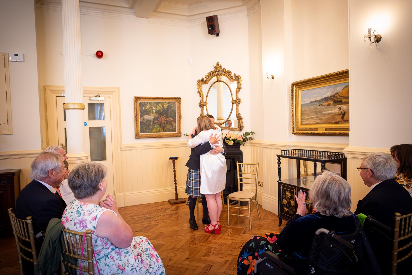 Clare and Sam hug surrounded by friends and family during their Civil Partnership in the Regency Room at Brighton Town Hall.