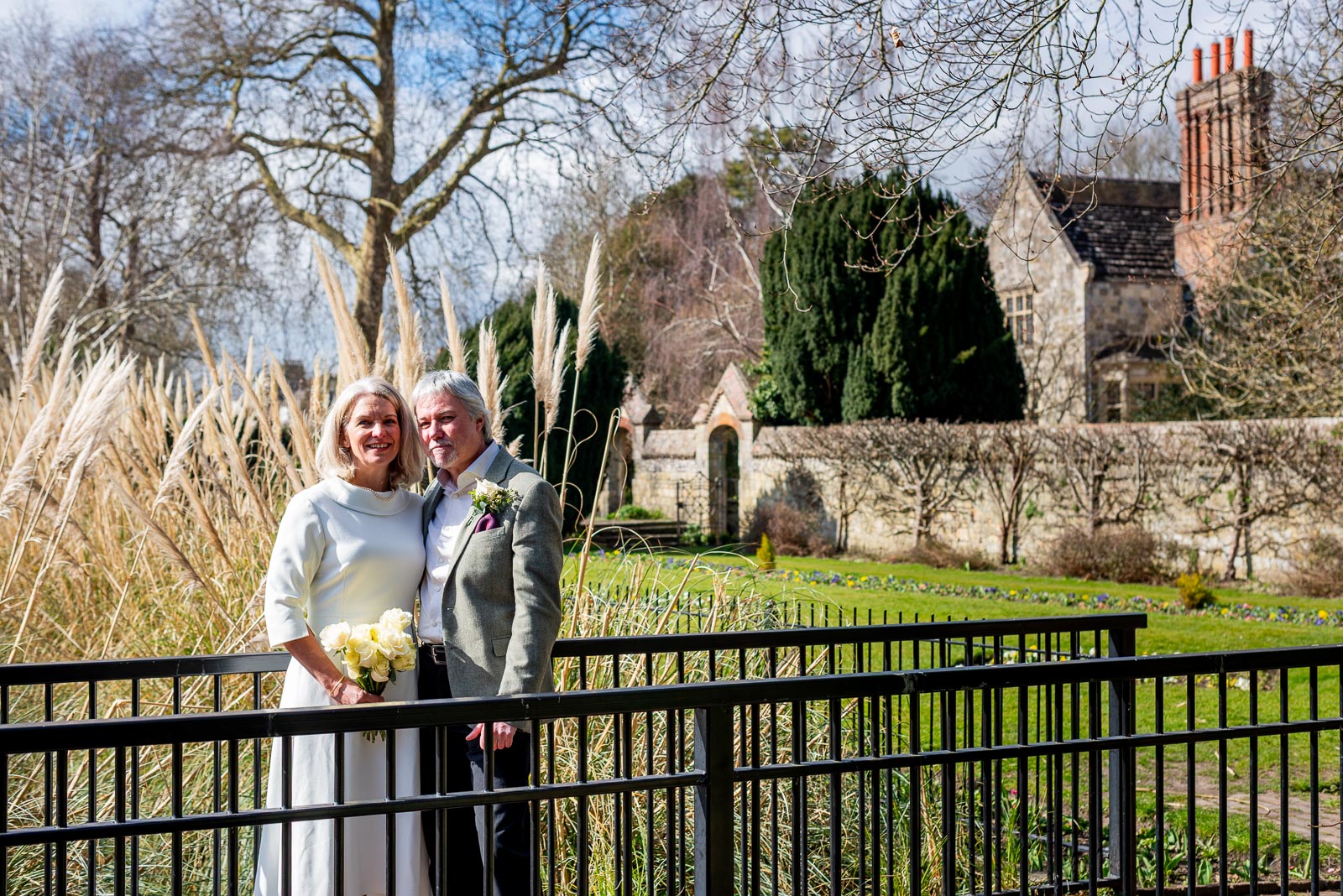 Jo and Darren hug on the bridge at Southover Grange with Lewes Registry Office in the background