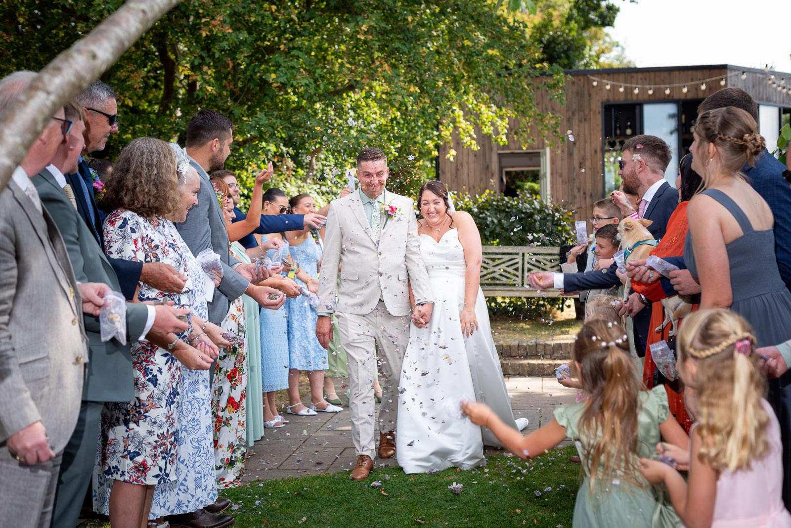 Tamsyn and Karl walk through confetti thrown by wedding guests in the Garden at The Jolly Sportsman in Chiltington near Lewes. 