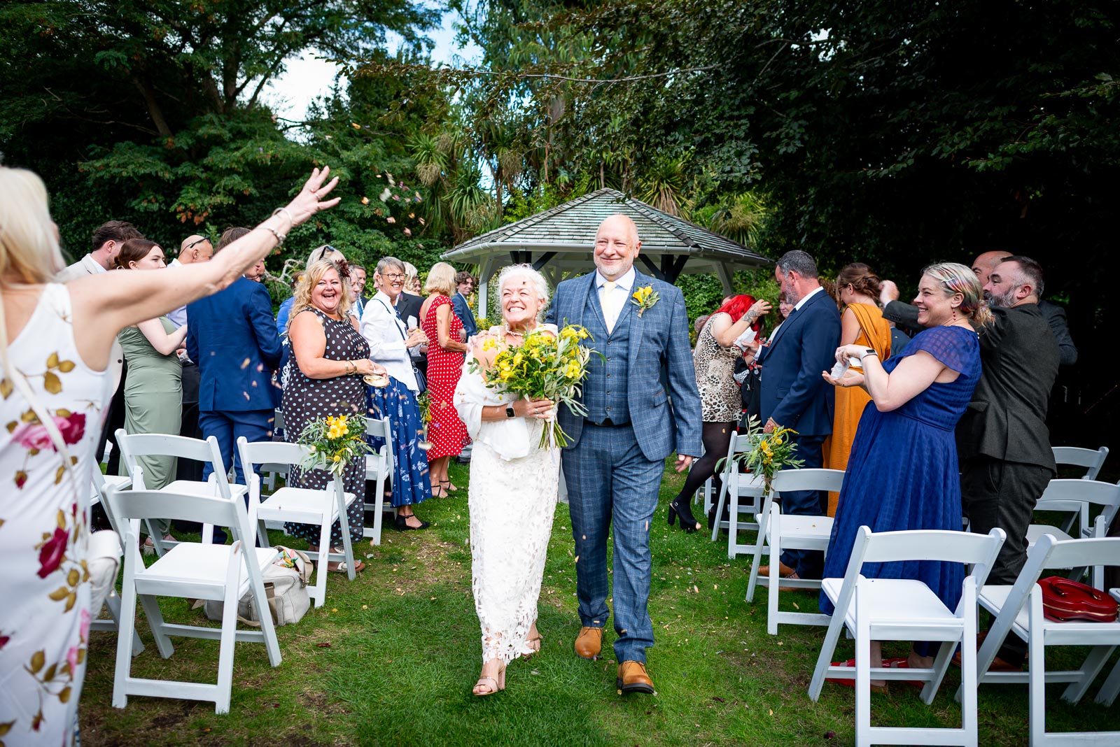 Karen and Hugh enjoy guests throwing  confetti whilst walking up the aisle after their wedding in the Gardens at Pelham House Hotel, Lewes.