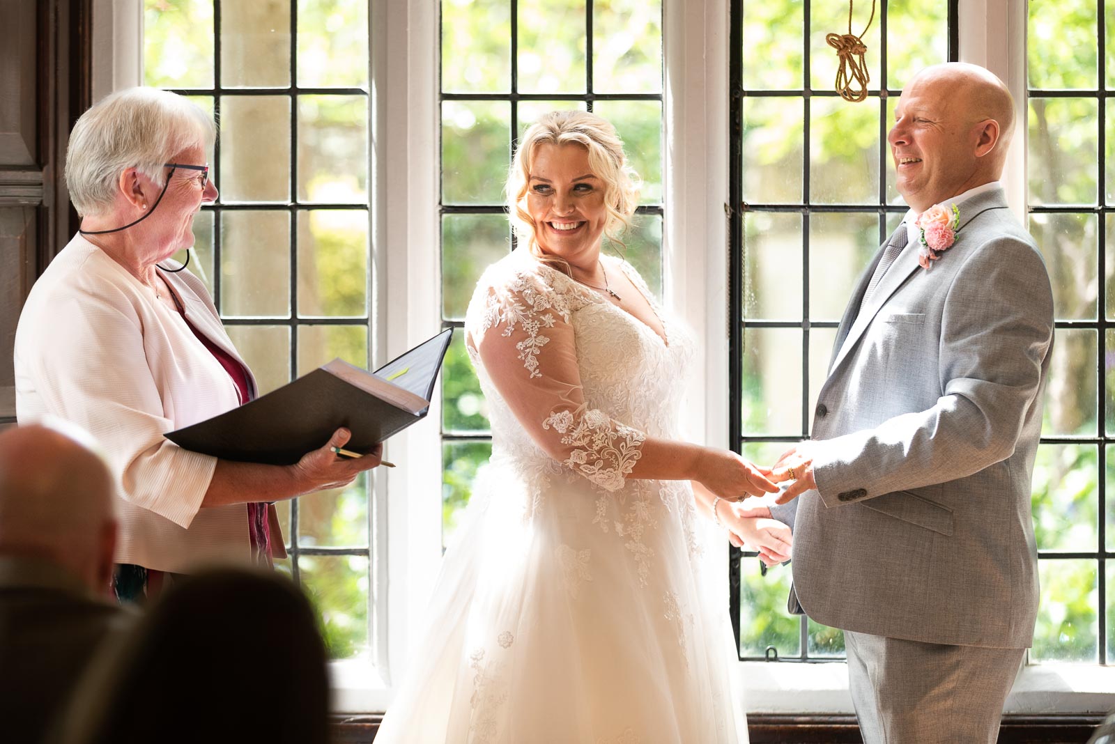 Lou and Matt laugh whilst standing at the top of the aisle in the Ainsworth Room at Lewes Register Office.